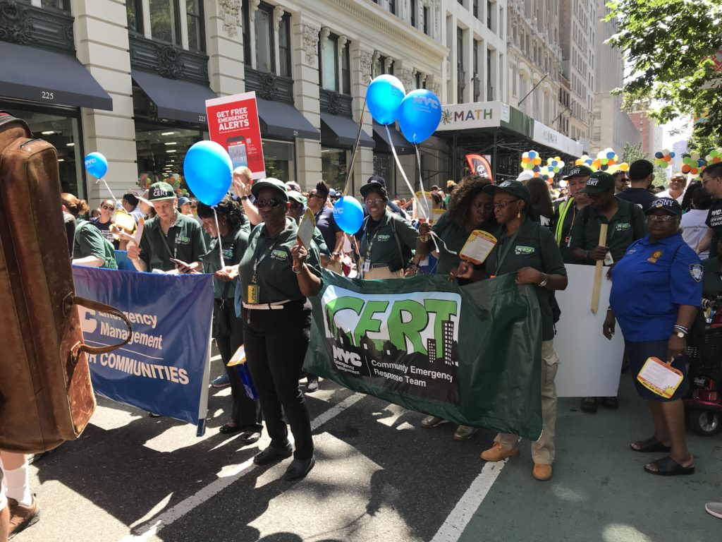 Multiple groups marching in the 2019 Disability Pride NYC Parade holding banners and blue balloons.