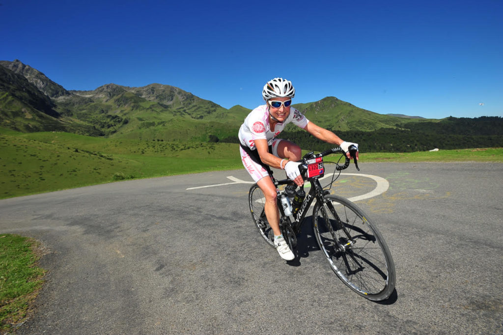 Christine Hemphill rides a bike wearing a helmet with a beautiful green hillside behind her