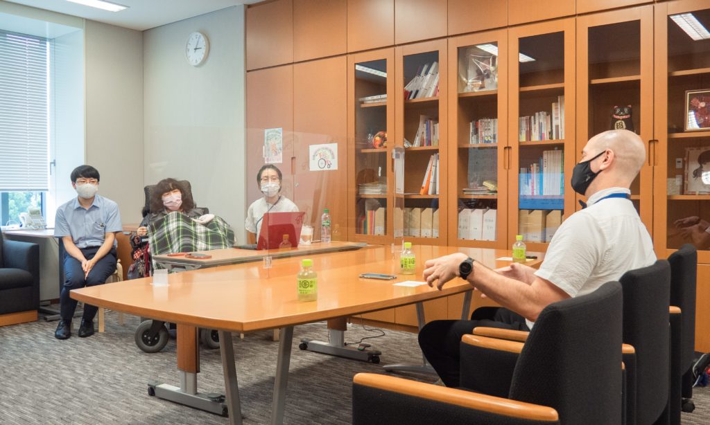 トマスローガンがテーブルの前に座り、電動車椅子に乗った木村英子氏が向かい側にいる。木村英子氏の両脇にアシスタントと秘書が座っている