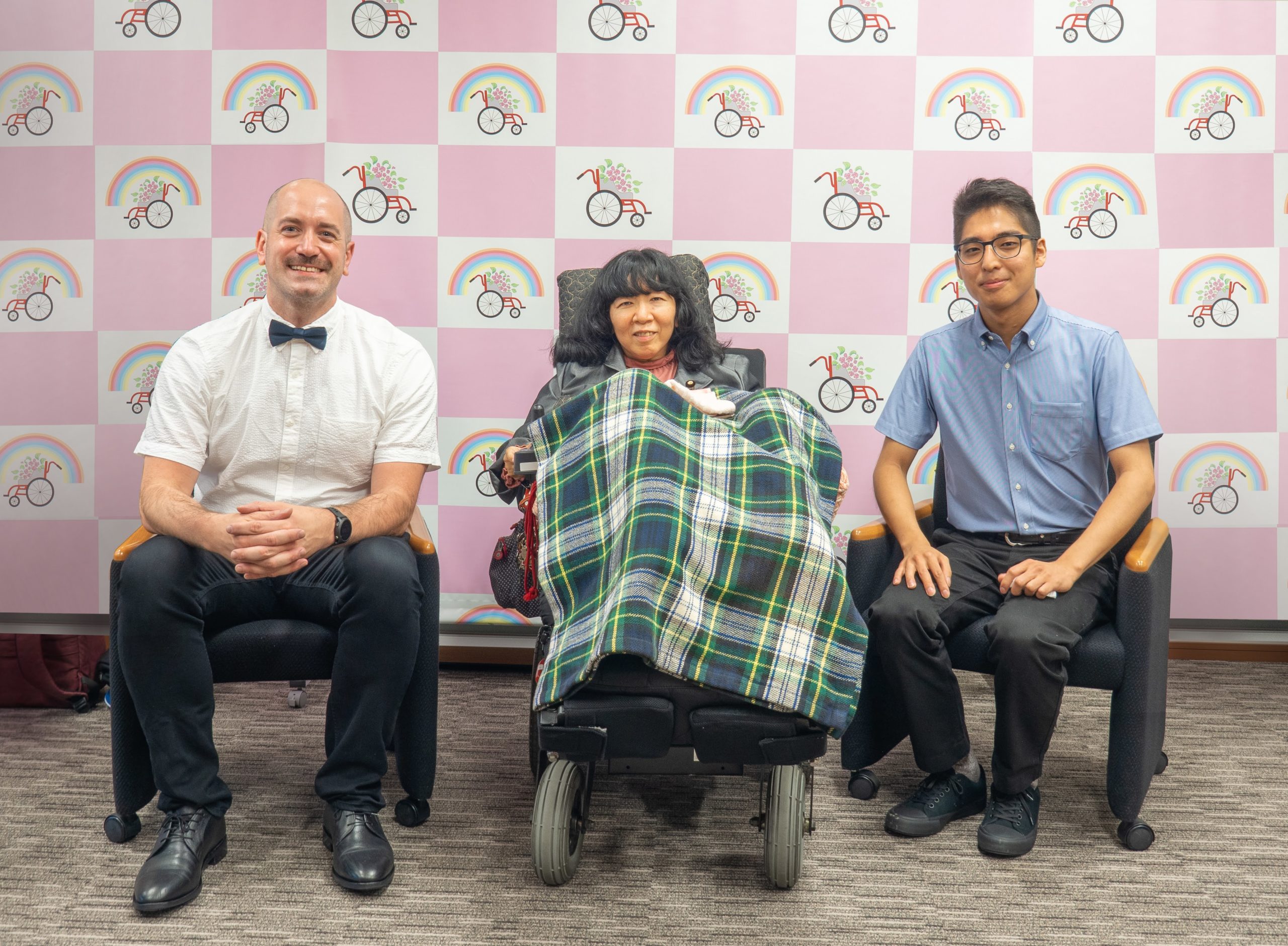 Thomas Logan sits next to Eiko Kimura in a wheelchair and Kenji Yanagawa sits on the other side of her
