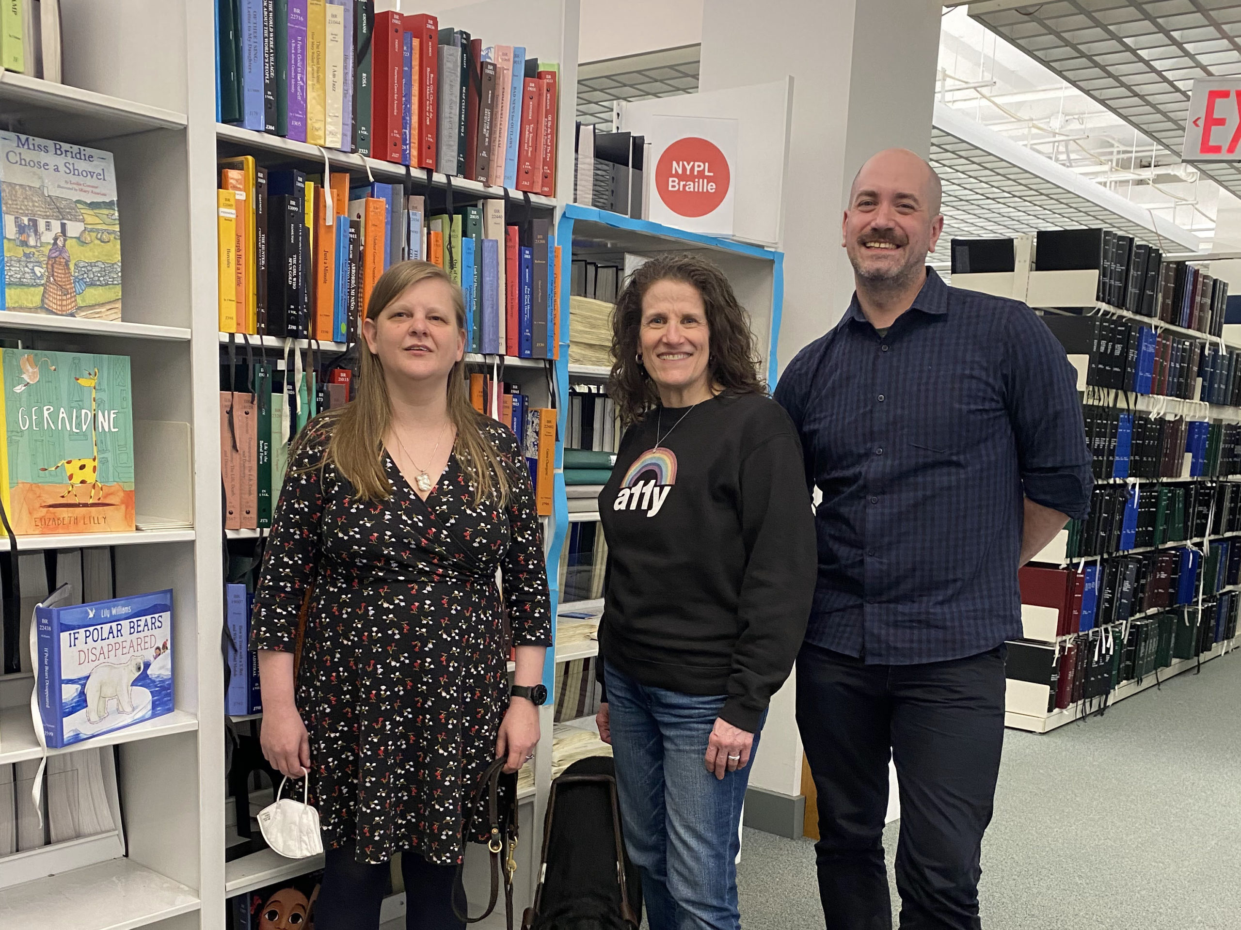 Chancey Fleet, Meryl Evans, and Thomas Logan stand in front of book stacks with Braille books