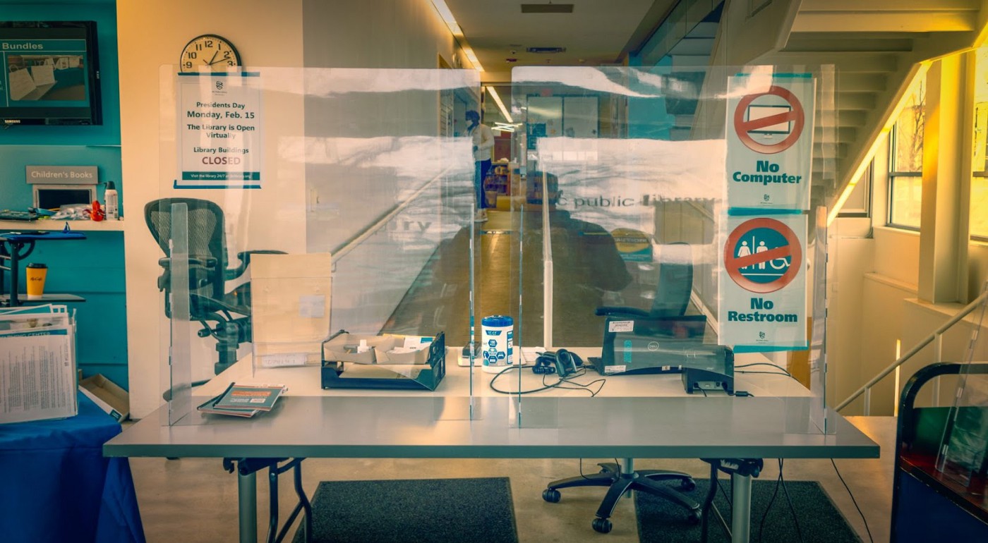 An empty medical office, with plexiglass barriers on top of a table in front, with signs saying “no computer” and “no restroom” Creator: Ted Eytan