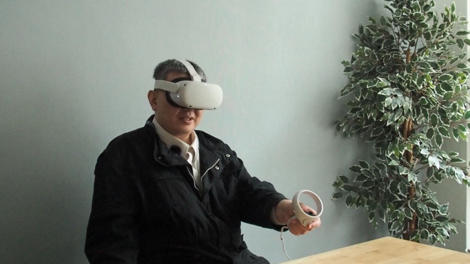 Katsutoshi wearing a white Meta headset and holding a hand controller in his left hand.