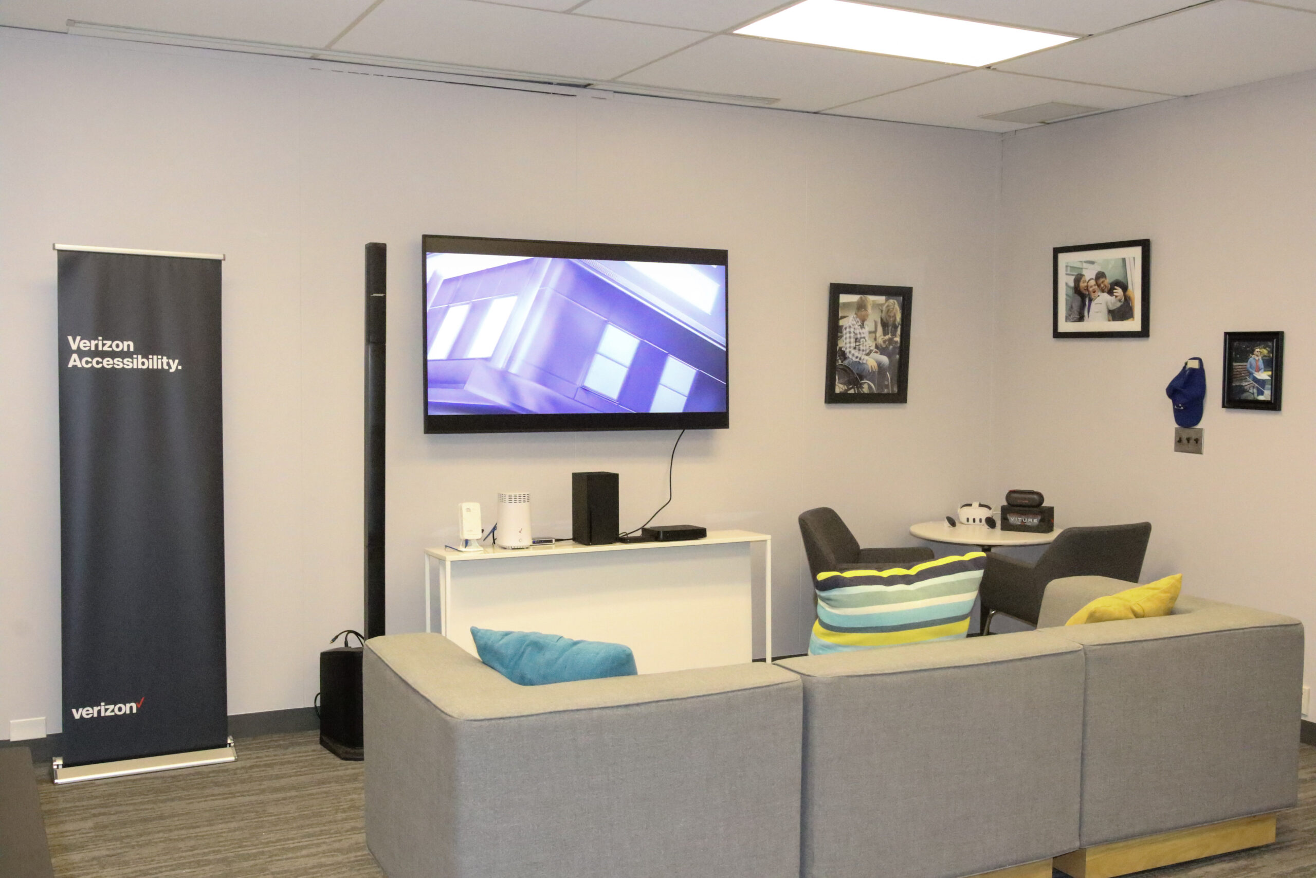 Verizon Home section with a sofa facing a big screen TV, a table top under the TV with Fios set-top box, extender, and gaming section with VR headsets.