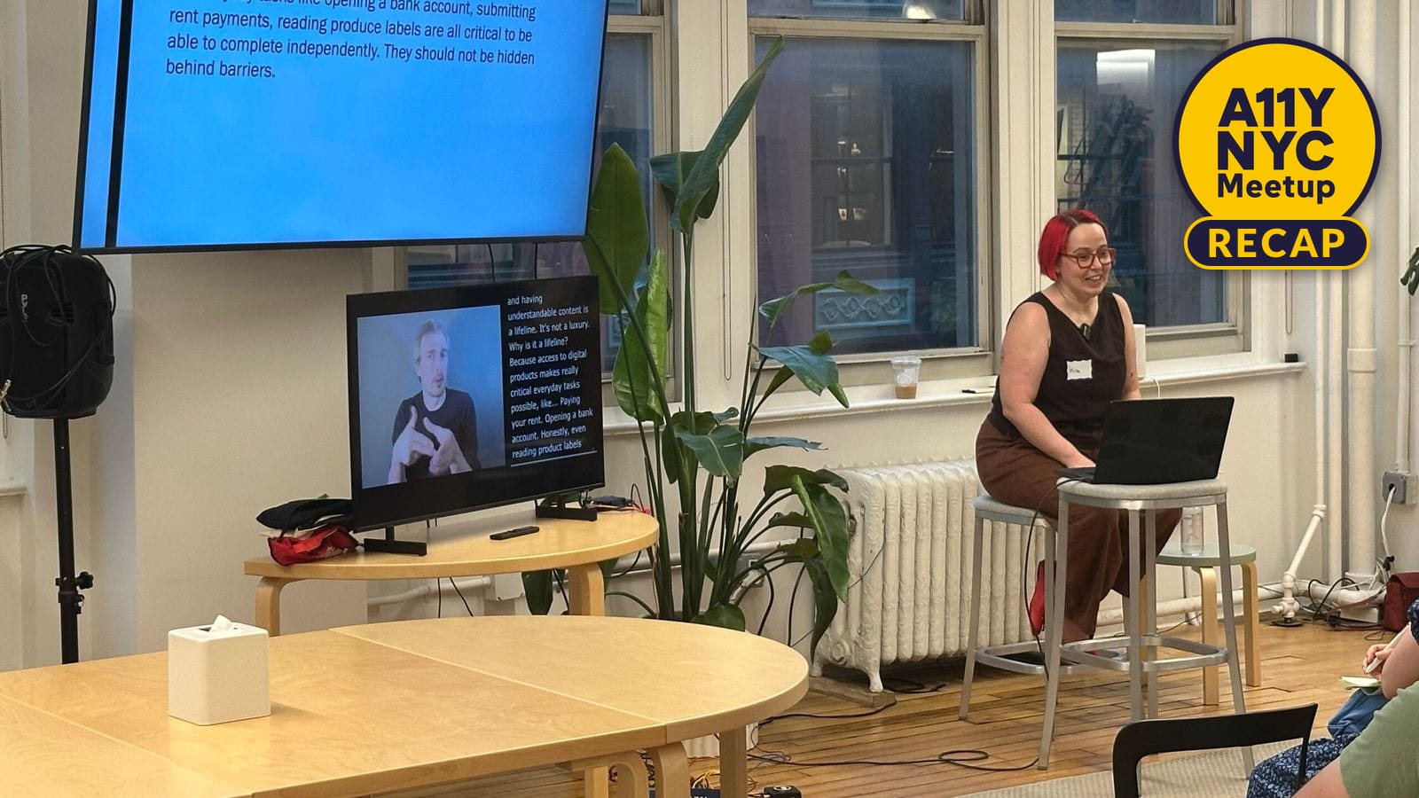 Irina Morozova sits on a stool with a laptop in front. To the side, is a big screen showing her current slide and a smaller screen beneath with ASL and captions.