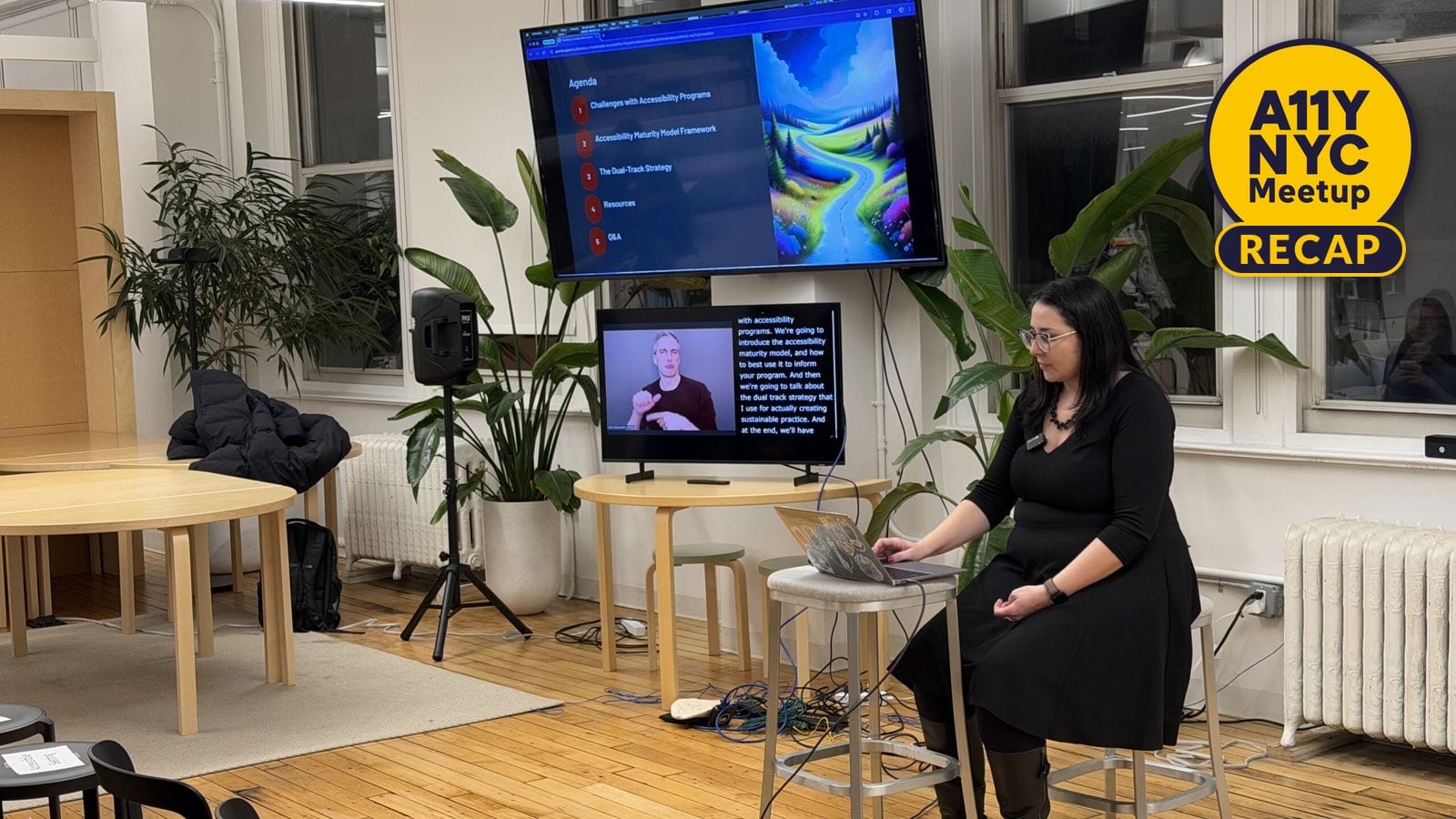 Lina sits on a stool in front of a laptop with a big screen to the side showing the presentation. Below is a smaller screen showing the ASL interpreter and captions.